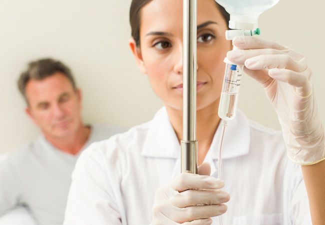 Медсестра в белом халате и стерильных перчатках внимательно регулирует капельницу с лекарством